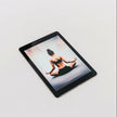 An Example product tablet rests on a white surface, showing a woman in workout clothes sitting cross-legged in a meditative yoga pose with her hands on her knees, viewed from behind.